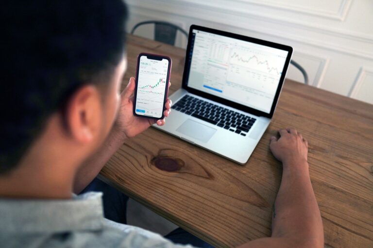 Investuotojas peržiūri rinkos grafikus telefone ir kompiuteryje, analizuodamas augimo ETF ir jų strategijas.