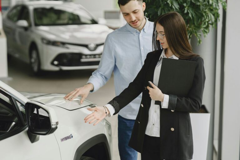 Automobilių salone klientas su konsultante apžiūri automobilį prieš pirkimą.