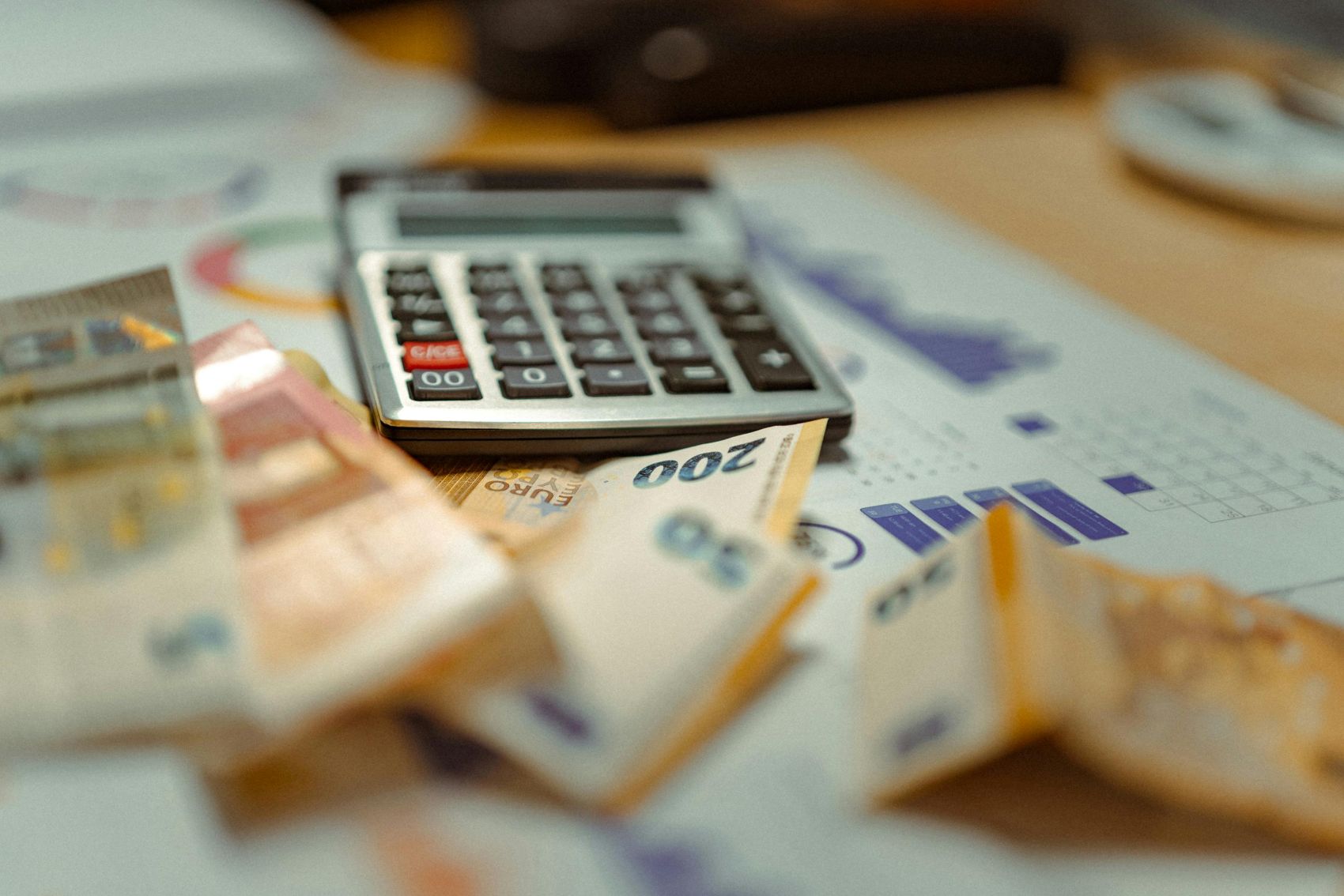 Skaičiuotuvas, euro banknotai ir finansiniai dokumentai ant stalo.