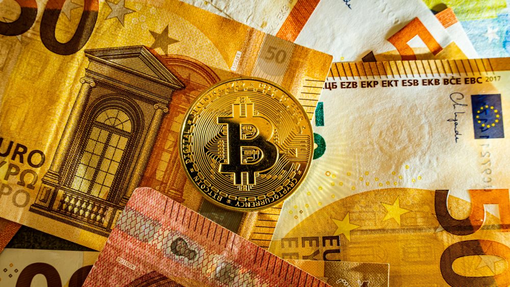 Bitcoin moneta padėta ant eurų banknotų – vizualus kriptovaliutų pavertimo į tradicinius pinigus (eurus) simbolis.