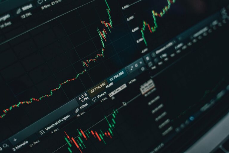 Kompiuterio ekrane matomas kylantis finansų rinkų grafikas su žaliomis ir raudonomis žvakėmis, iliustruojantis investavimo strategijas ir rinkos analizę.