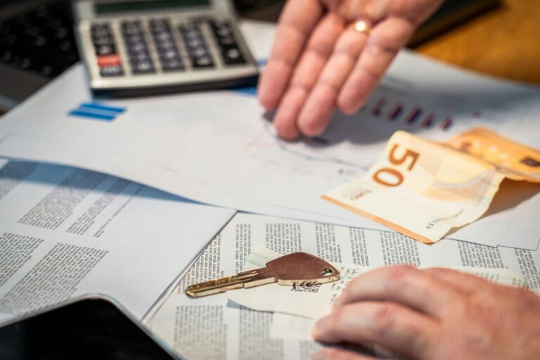 Dokumentai, skaičiuotuvas, 50 eurų banknotas ir raktas ant stalo, simbolizuojantys verslo liudijimo veiklą ir su ja susijusius mokėjimus.